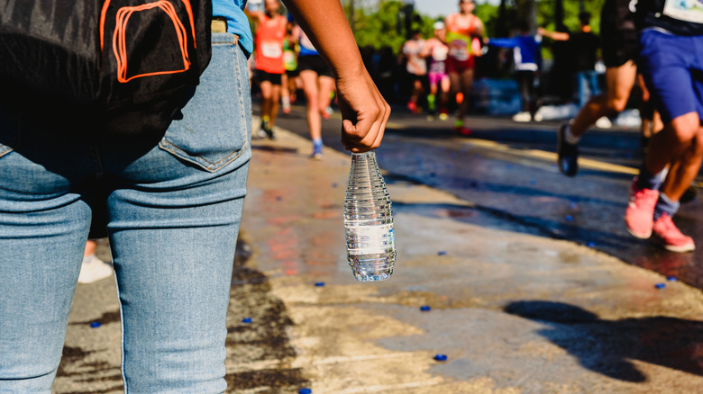 back view of a person with backpack holding water bottle while people exercise