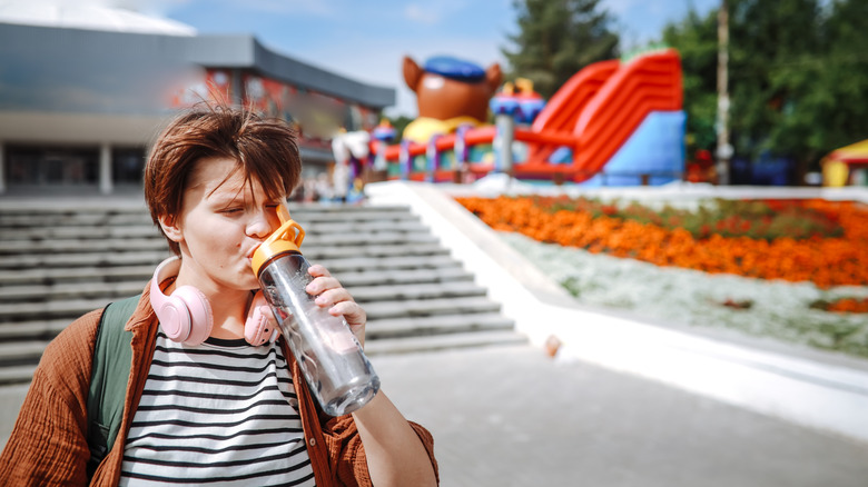 teenager with backpack and headphones around their neck while drinking from water bottle