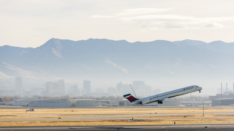 A commercial jet taking off from SLC Airport with Salt Lake City in the background.
