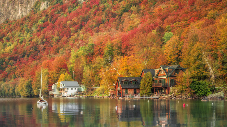 A cabin on the shore of Lake Willoughby surrounded by fall leaves and a sailboat on the water