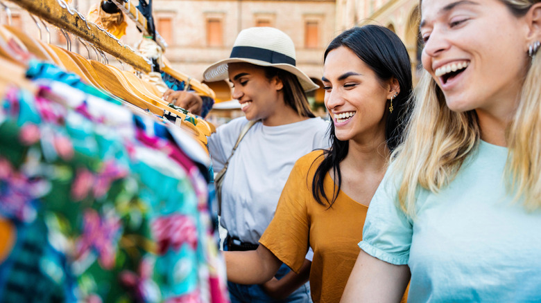 Women happily browse clothing racks in a street