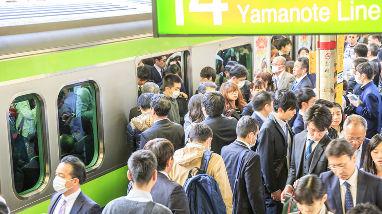 Crowd of commuters getting on and off a train at rush hour in Shinjuku Station.