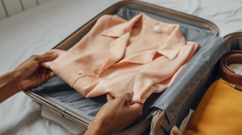 Hands placing clothes in a suitcase.