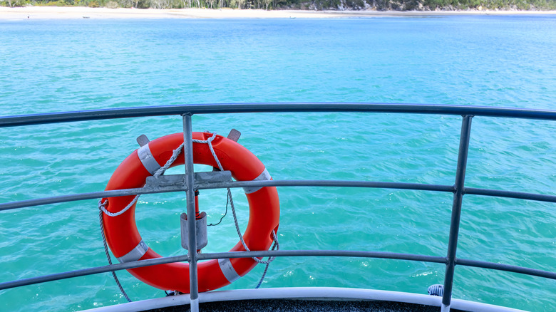 An orange life buoy hanging on a ship railing against the blue ocean.