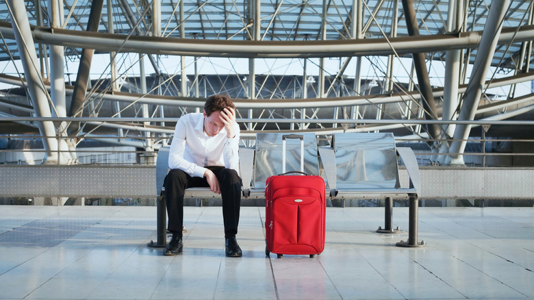 Man sitting with head in hand at airport with red luggage