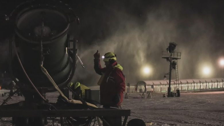 Resort worker stands near snow machine as it produces snow throughout the night