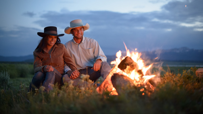 couple wearing cowboy hats by campfire