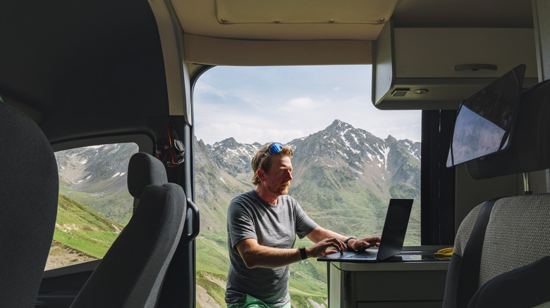 man working on his computer from his van in the mountains