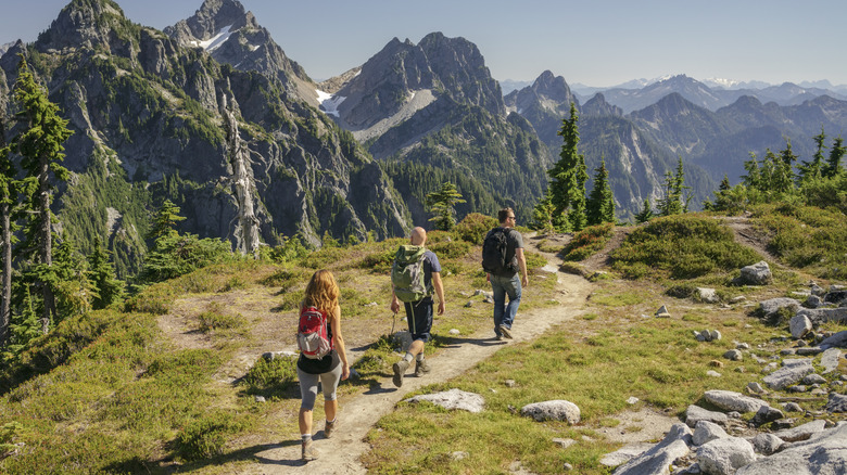 Three hikers walk along a path with mountains in the background.
