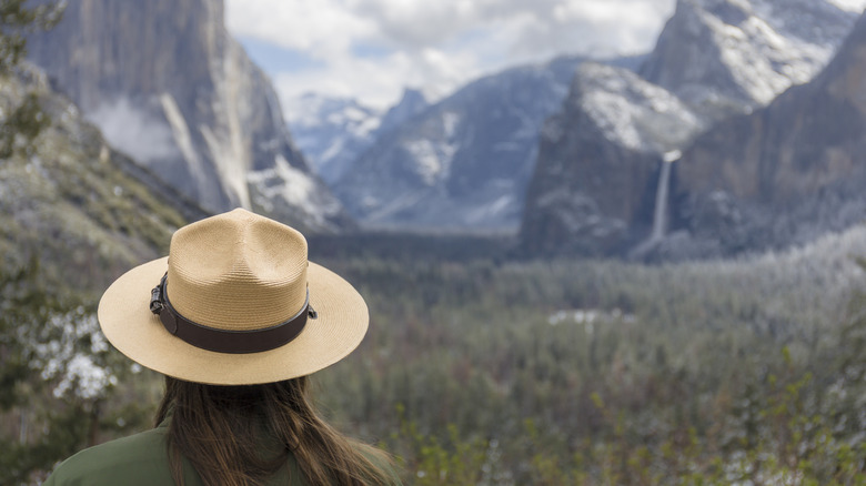 A park ranger wearing a hat looks out at scenic mountains.