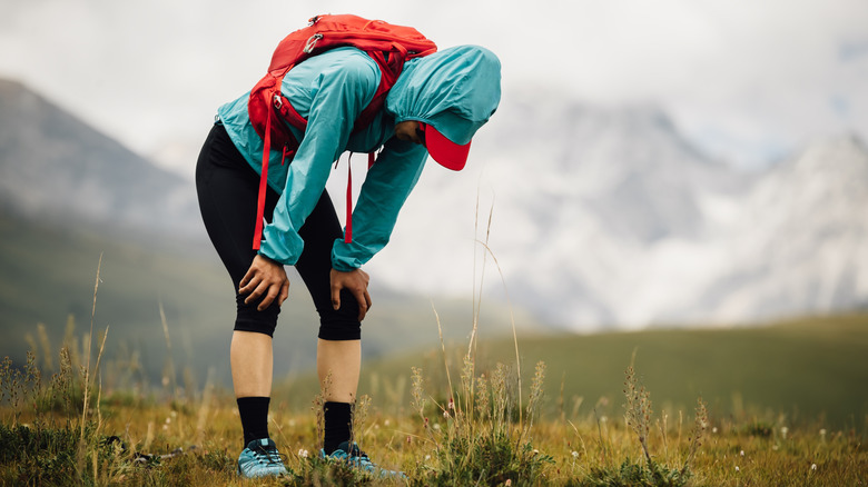 Tired woman in the mountains bends over her knees