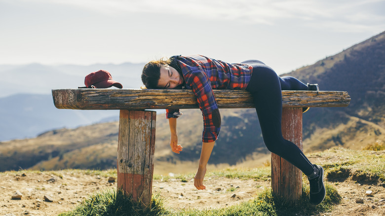 Completely tired and worn out woman lays on bench on a hike