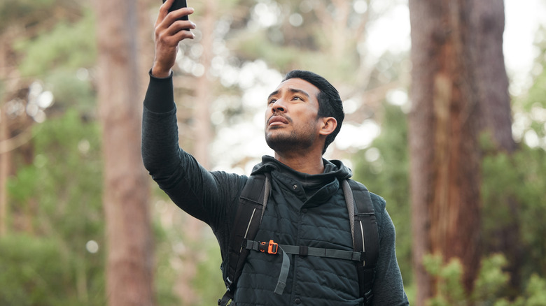 hiker with backpack in the forest stressed holding his phone due to bad connection