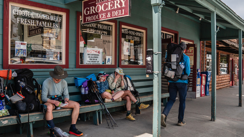 Backpackers rest on benches in front of a deli
