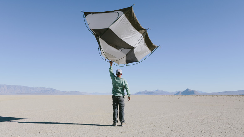A man holds up a tent in the middle of the desert