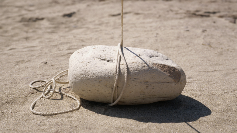 A rock resting on sandy surface is tied up with rope