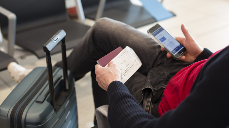 A man holding a boarding pass and passport in one hand and his cell phone in the other.