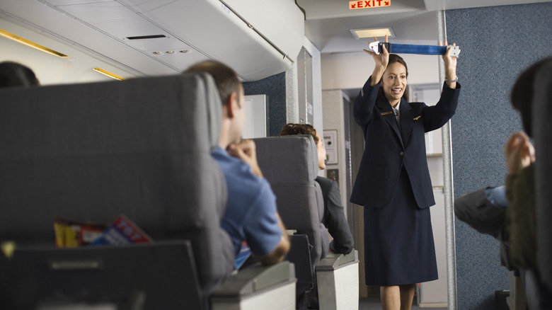 A flight attendant demonstrates a seatbelt to passengers on an airplane.