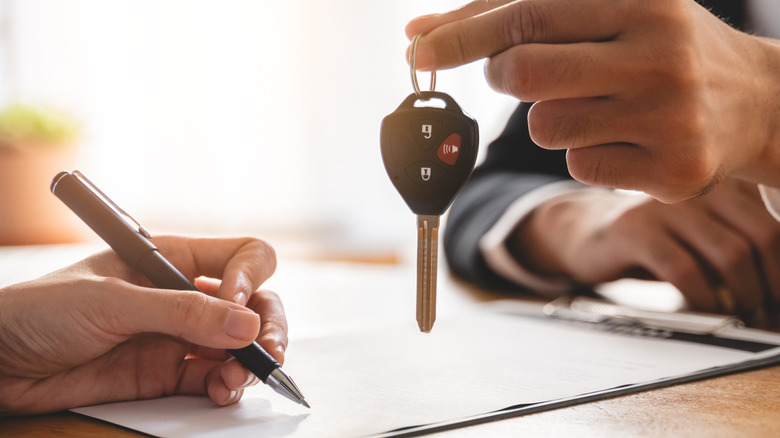 hand of car dealer holding car key while the customer sign document