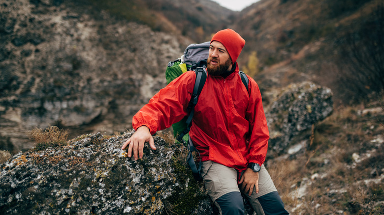 A male hiker in a red waterproof jacket taking a rest by a rock
