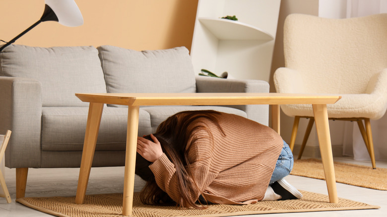 A person taking cover under a table during an earthquake.
