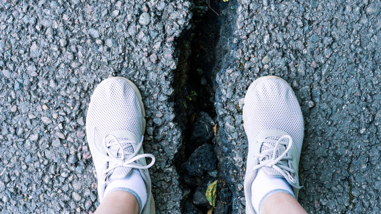 Feet on either side of a cracked sidewalk affected by an earthquake.