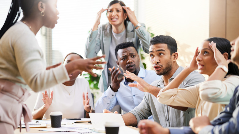 A group of people having a conversation and gesturing around a table.