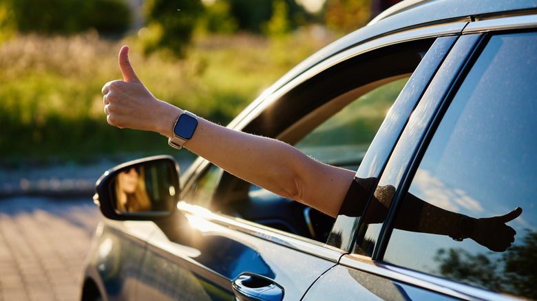 A person giving thumbs up out of a car window.