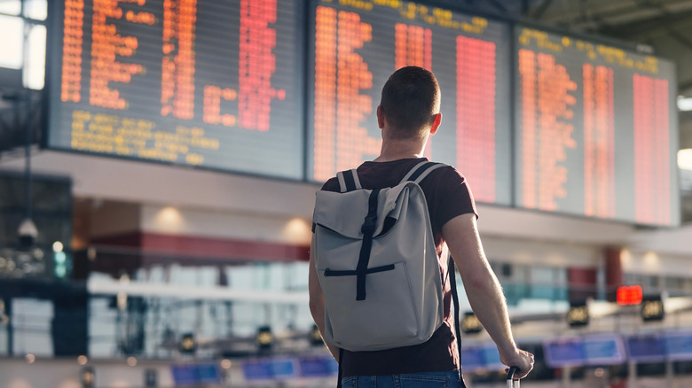 man with backpack looking at departure board