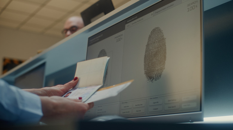 Hands comparing a passport to a computer screen with a fingerprint on it.