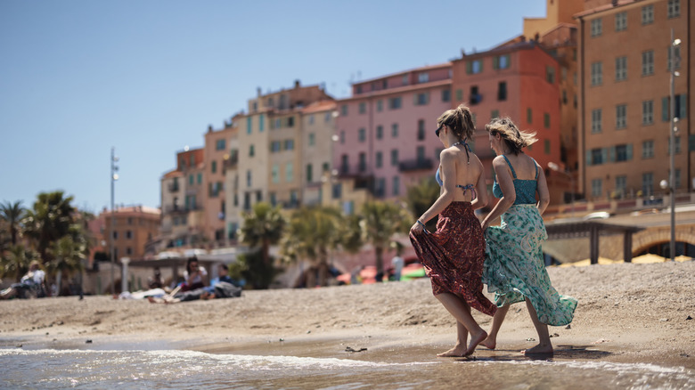 Two women walking on the sand on a beach in Menton