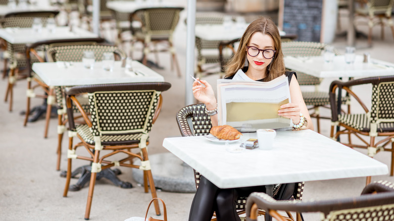 A women reading a paper while smoking at a café