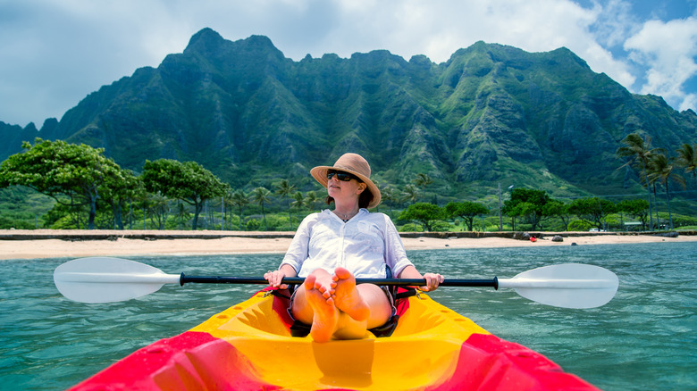 A woman sits in a kayak in front of Hawaiian mountains