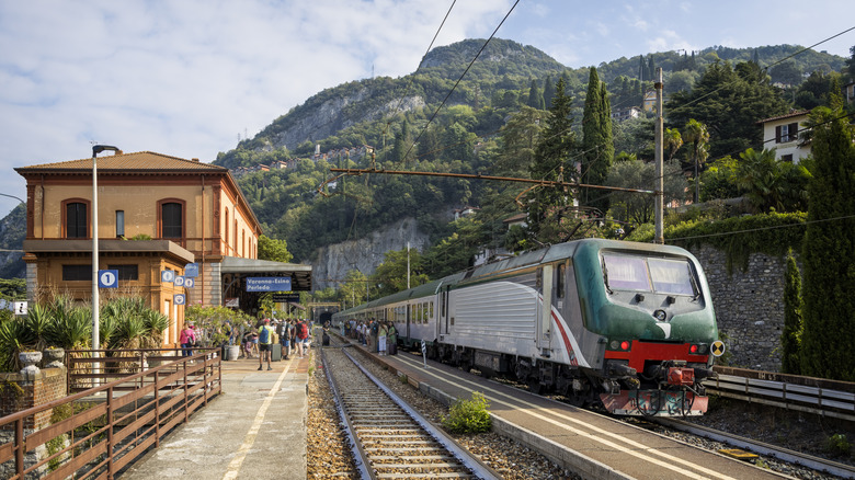 A train sitting at the platform waiting for passengers to board with mountains in the background