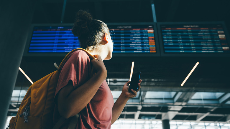 A woman checking the airline schedule board at an airport.