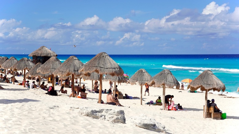 Tourists under palapas on a beach near Cancun