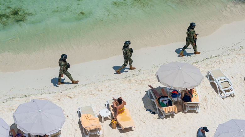 Mexican soliders patroling past umbrellas and loungers on Cancun beach
