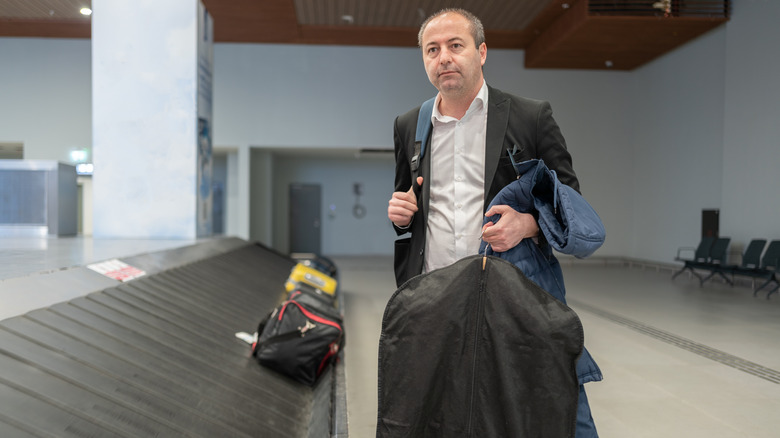 A man holds a garment bag near a luggage carousel