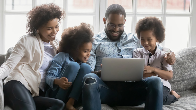 A woman, man, and two children on a couch with a laptop, making travel reservations.