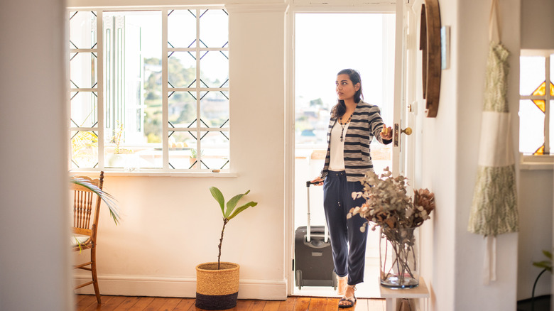 A young woman with luggage opens the door to her rental accommodation.
