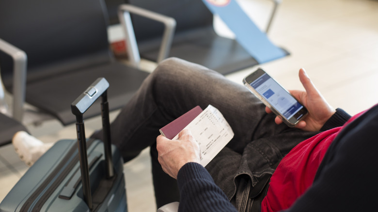 Someone checks their flight details on their phone while holding a ticket and passport