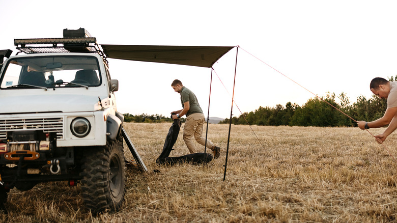 People setting up an awning off a parked camper vehicle.