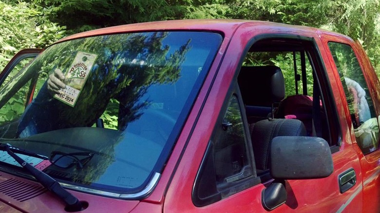 A man hangs a Washtingston State Discover Pass in his red pickup truck