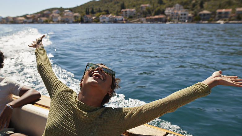 Happy young woman with arms raised on motorboat enjoying a sunny day.