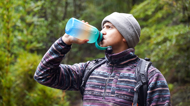 a hiker drinking rainwater from a blue plastic bottle
