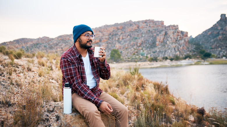 man drinks coffee by a lake
