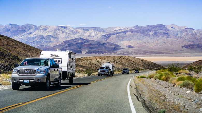 A row of trucks and cars with trailers driving along the highway in Death Valley