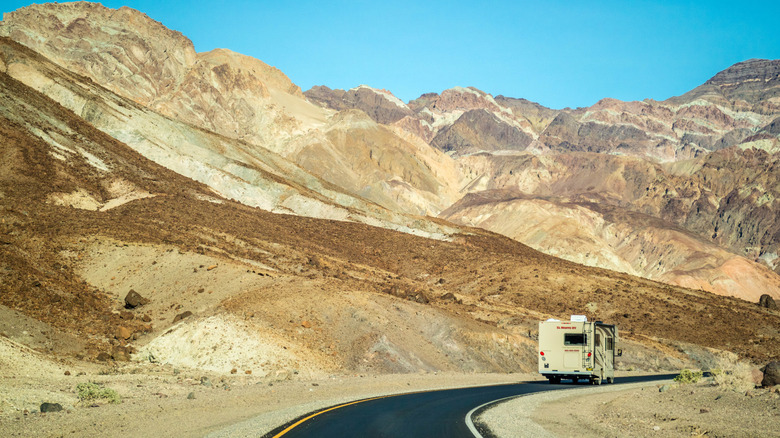 An RV driving around a bend of a highway with mountains and desert