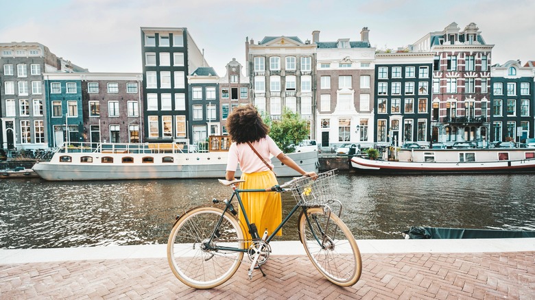 woman with bike looks at buildings, boats, and canal