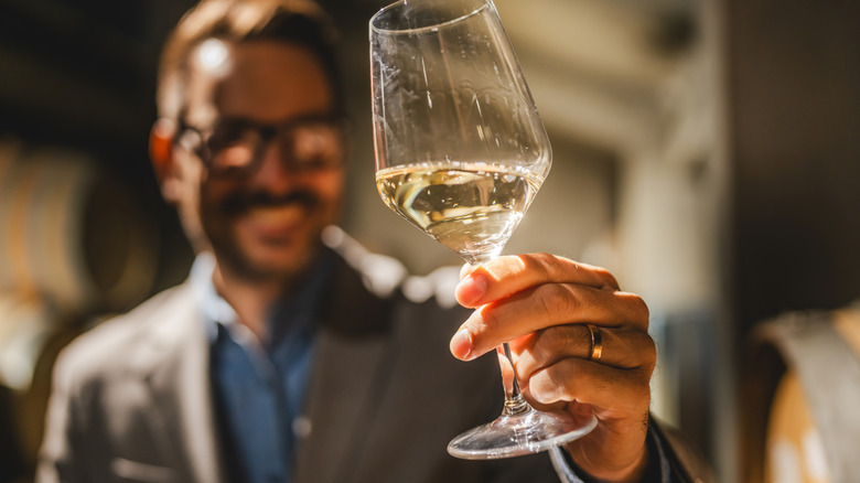 A wine glass in focus in the foreground while a man in the background examines it.